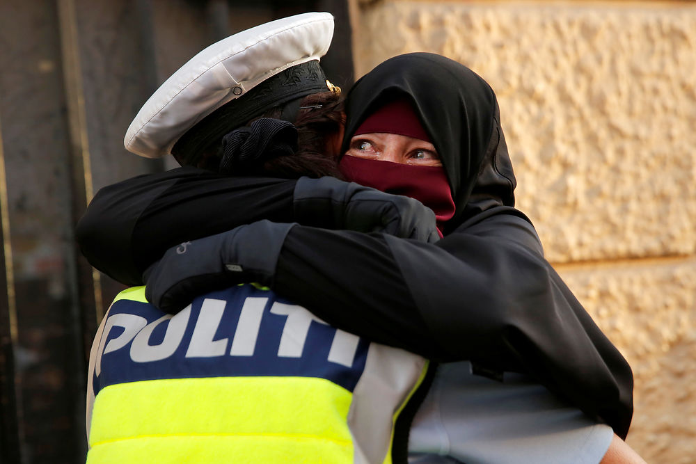 Ayah, a wearer of the niqab weeps as she is embraced by a police officer during a demonstration against the Danish face veil ban in Copenhagen